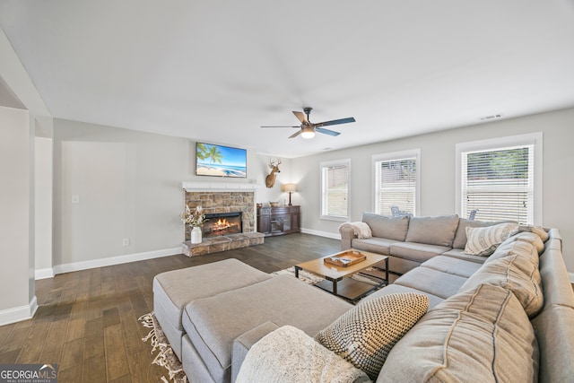 living room featuring ceiling fan, dark hardwood / wood-style floors, and a stone fireplace