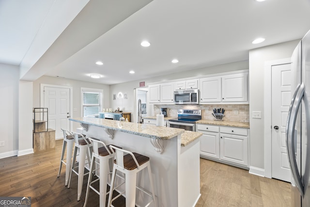 kitchen featuring appliances with stainless steel finishes, backsplash, light stone counters, white cabinets, and a center island