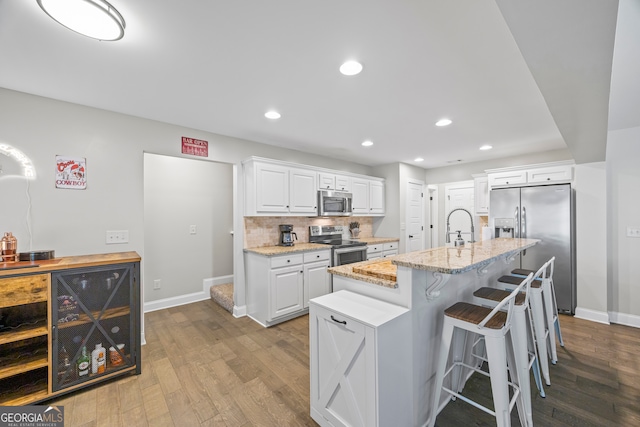 kitchen with white cabinets, light stone countertops, an island with sink, stainless steel appliances, and beverage cooler