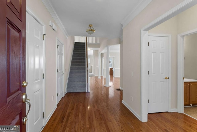 hallway featuring crown molding, baseboards, stairs, wood finished floors, and decorative columns