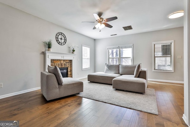 living room with a stone fireplace, ceiling fan, and wood-type flooring