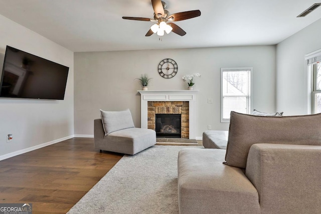 living room featuring ceiling fan, a fireplace, and dark wood-type flooring