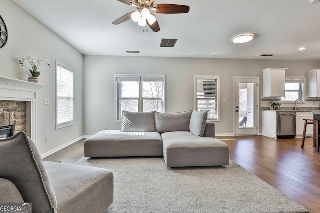 living room with dark hardwood / wood-style floors, a stone fireplace, ceiling fan, and sink