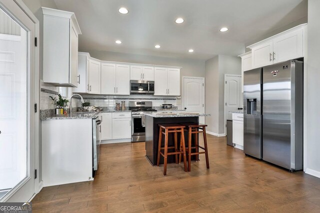 kitchen featuring a kitchen island, light stone counters, white cabinetry, and stainless steel appliances