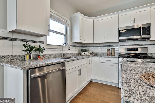 kitchen featuring white cabinetry, sink, stainless steel appliances, light stone counters, and hardwood / wood-style flooring