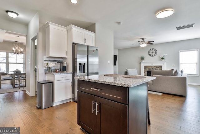 kitchen featuring light stone counters, ceiling fan with notable chandelier, stainless steel fridge with ice dispenser, white cabinetry, and a stone fireplace