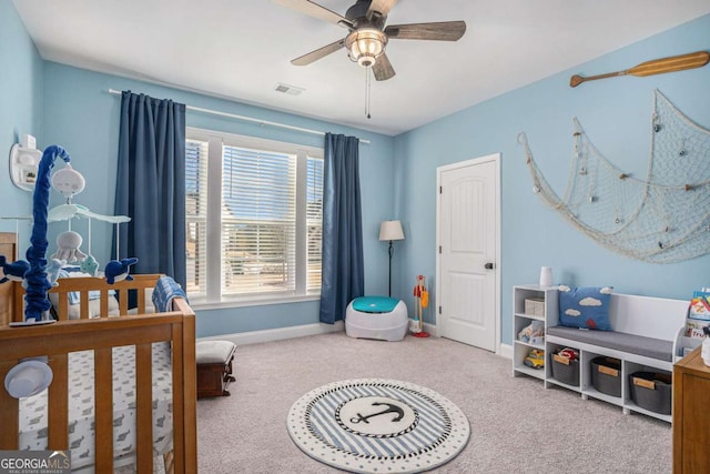 carpeted bedroom with ceiling fan, multiple windows, and a nursery area