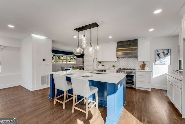 kitchen with white cabinetry, an island with sink, stainless steel range, tasteful backsplash, and decorative light fixtures