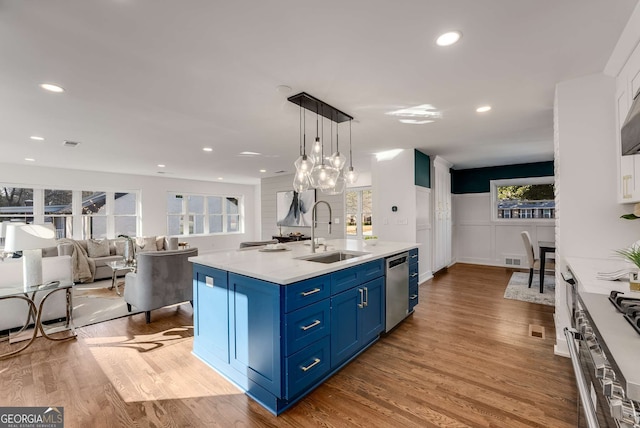 kitchen featuring dishwasher, a center island with sink, sink, hanging light fixtures, and blue cabinetry