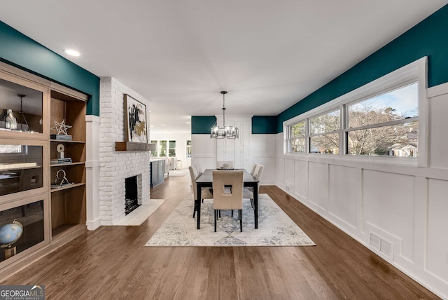 dining space with a brick fireplace, dark hardwood / wood-style flooring, and a notable chandelier