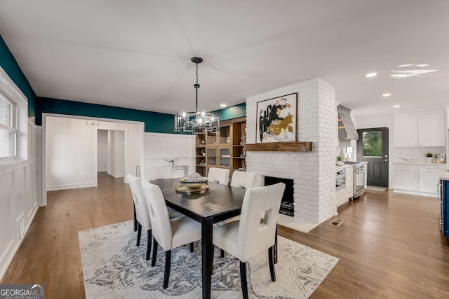 dining space with a fireplace, an inviting chandelier, and light hardwood / wood-style floors