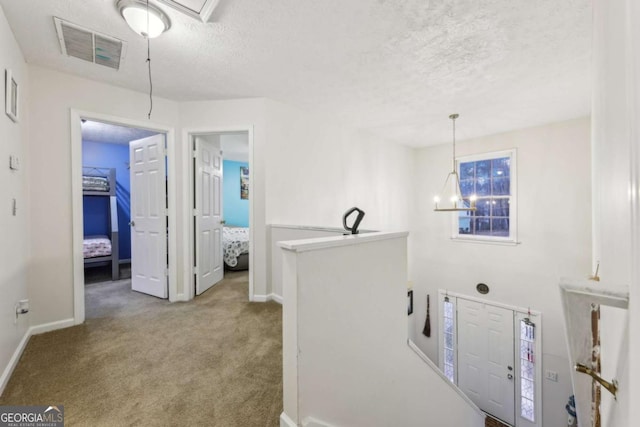 hall with light carpet, a textured ceiling, and a chandelier