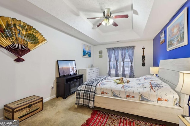 carpeted bedroom featuring a tray ceiling, ceiling fan, and a textured ceiling