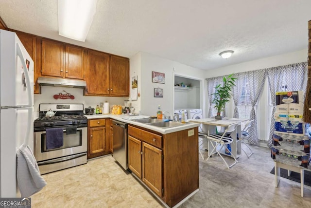 kitchen featuring sink, washing machine and dryer, a textured ceiling, appliances with stainless steel finishes, and kitchen peninsula