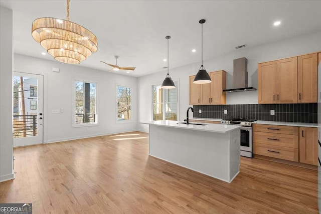 kitchen featuring ceiling fan with notable chandelier, wall chimney range hood, sink, gas range, and decorative light fixtures