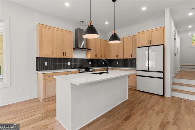 kitchen featuring wall chimney exhaust hood, sink, light brown cabinets, white fridge, and hanging light fixtures