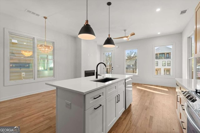 kitchen with a kitchen island with sink, white cabinets, sink, appliances with stainless steel finishes, and decorative light fixtures