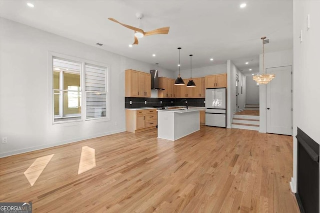 kitchen featuring a center island with sink, wall chimney range hood, sink, hanging light fixtures, and white fridge