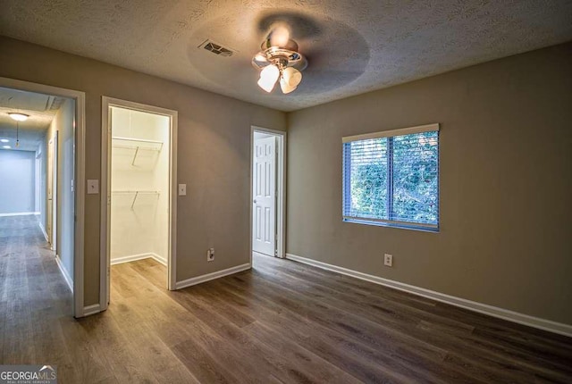 unfurnished bedroom featuring a textured ceiling, a walk in closet, a closet, and ceiling fan