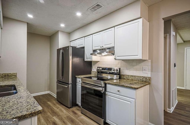 kitchen featuring white cabinetry, backsplash, hardwood / wood-style floors, dark stone counters, and appliances with stainless steel finishes