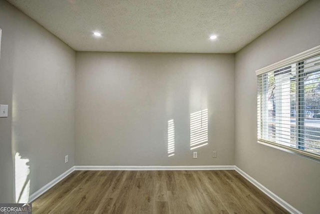 spare room with a wealth of natural light, a textured ceiling, and hardwood / wood-style flooring