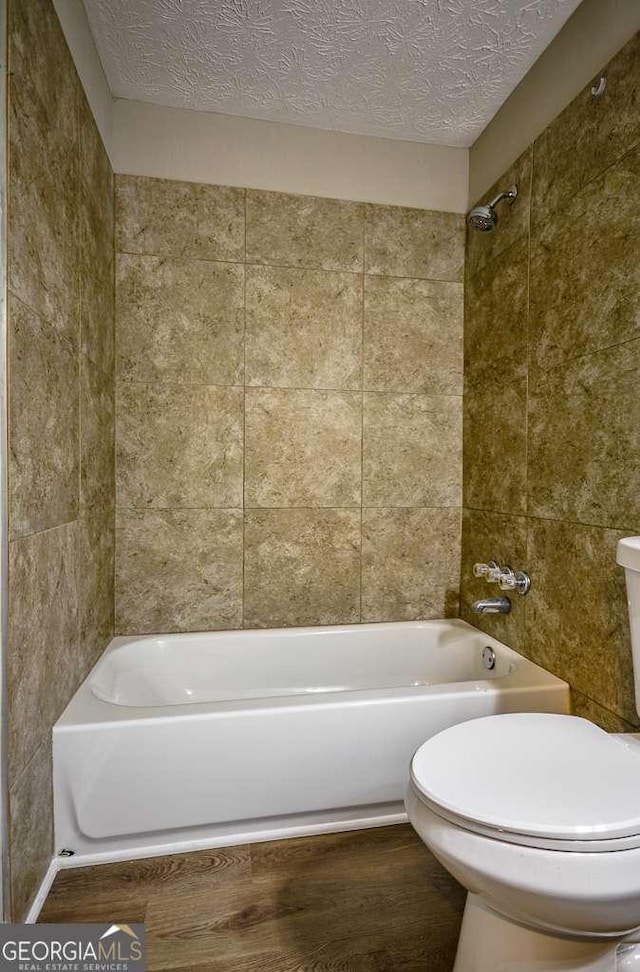 bathroom featuring a textured ceiling, tiled shower / bath combo, wood-type flooring, tile walls, and toilet