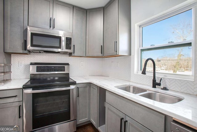 kitchen featuring light stone countertops, sink, stainless steel appliances, tasteful backsplash, and gray cabinets