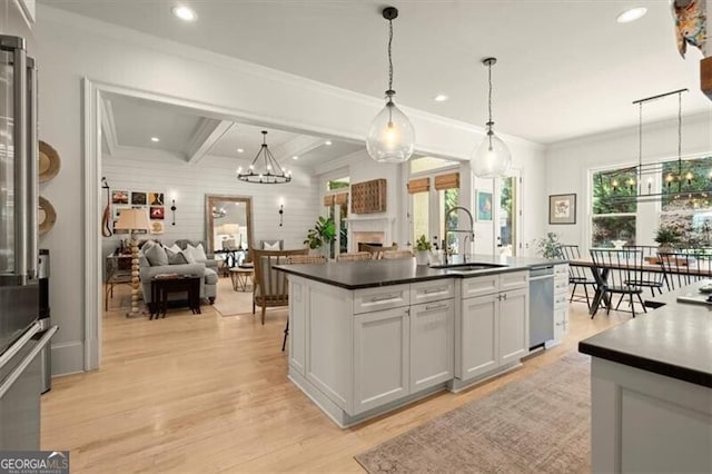 kitchen with a kitchen island with sink, sink, beamed ceiling, decorative light fixtures, and light hardwood / wood-style floors