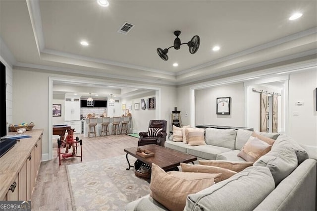 living room featuring ceiling fan, light hardwood / wood-style floors, ornamental molding, and a tray ceiling