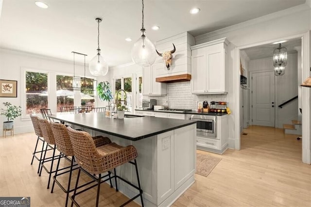 kitchen with white cabinets, sink, an island with sink, appliances with stainless steel finishes, and decorative light fixtures