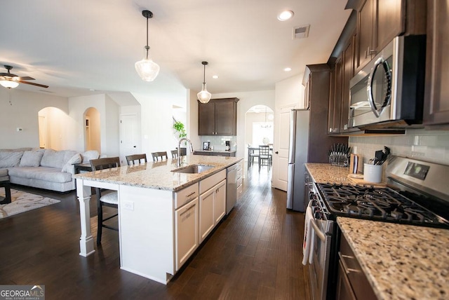 kitchen with sink, a kitchen island with sink, a breakfast bar, dark brown cabinets, and appliances with stainless steel finishes