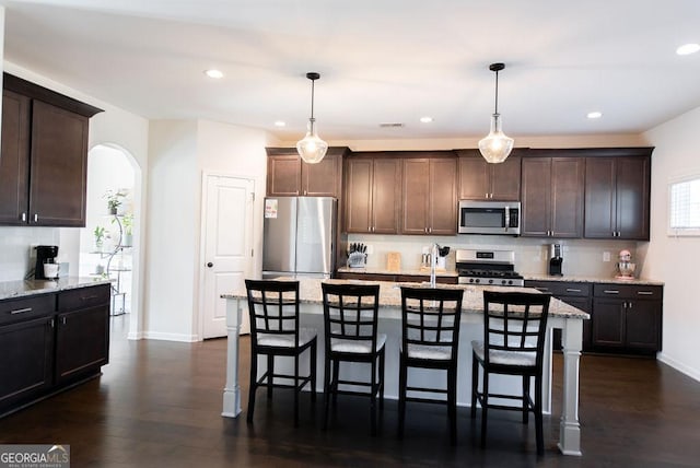 kitchen featuring light stone countertops, appliances with stainless steel finishes, a center island, and hanging light fixtures