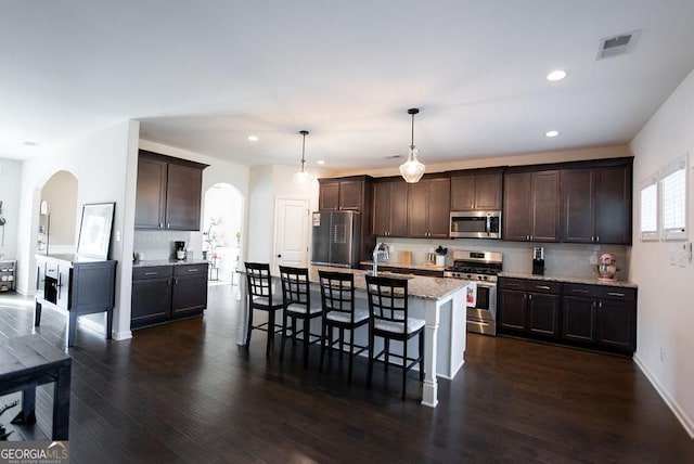 kitchen with decorative backsplash, stainless steel appliances, a kitchen island with sink, decorative light fixtures, and dark hardwood / wood-style floors