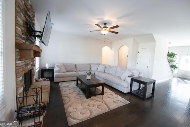 living room featuring dark hardwood / wood-style floors, ceiling fan, and a stone fireplace