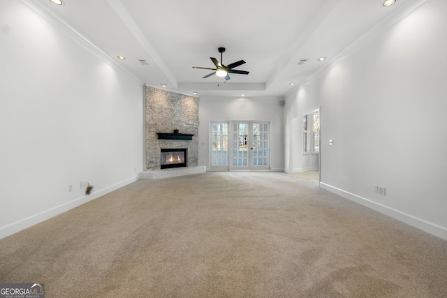 unfurnished living room with ceiling fan, french doors, light colored carpet, a tray ceiling, and a fireplace