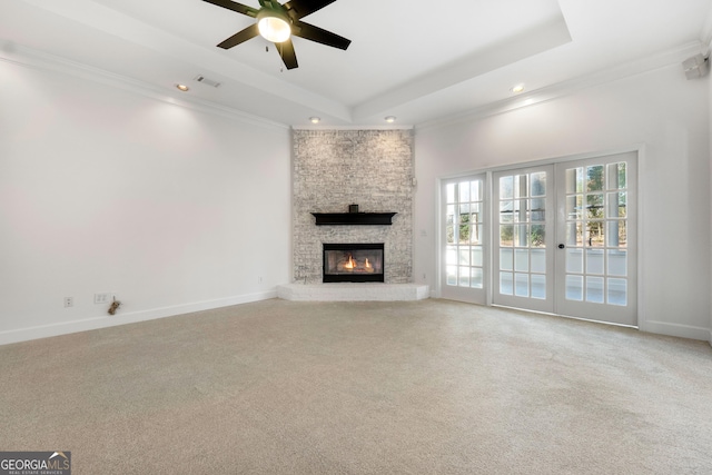 unfurnished living room featuring carpet flooring, ceiling fan, french doors, a stone fireplace, and a tray ceiling