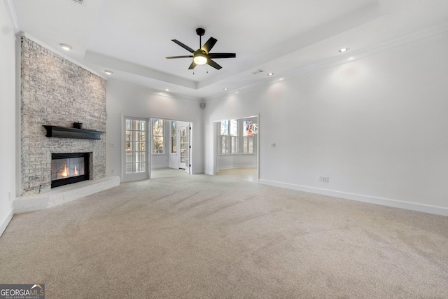 unfurnished living room featuring a raised ceiling, ceiling fan, a fireplace, and light colored carpet