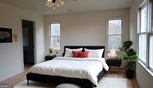 bedroom with light wood-type flooring, ensuite bath, and a notable chandelier