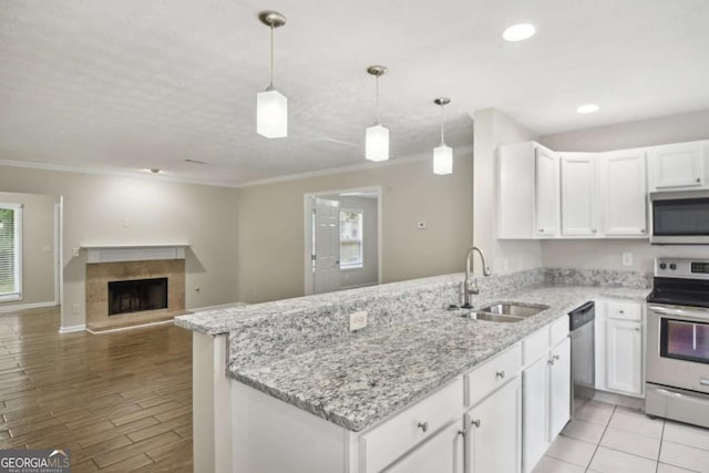 kitchen with stainless steel appliances, sink, white cabinetry, hanging light fixtures, and a tiled fireplace