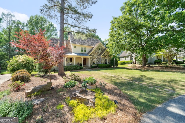 view of front of property with a front lawn, stone siding, a chimney, metal roof, and covered porch