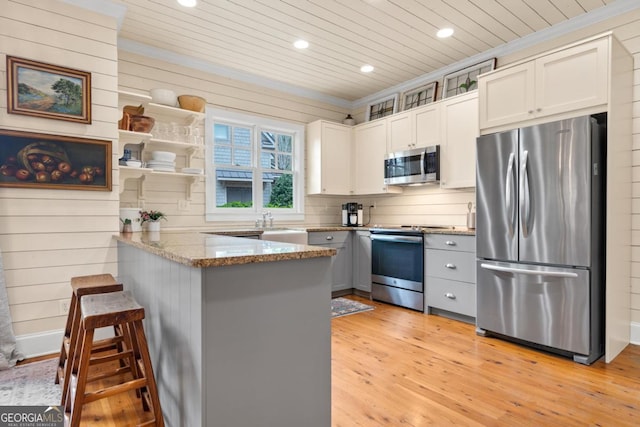 kitchen with a kitchen breakfast bar, white cabinetry, kitchen peninsula, and appliances with stainless steel finishes