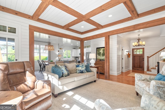 living area with beamed ceiling, light wood finished floors, stairs, and an inviting chandelier
