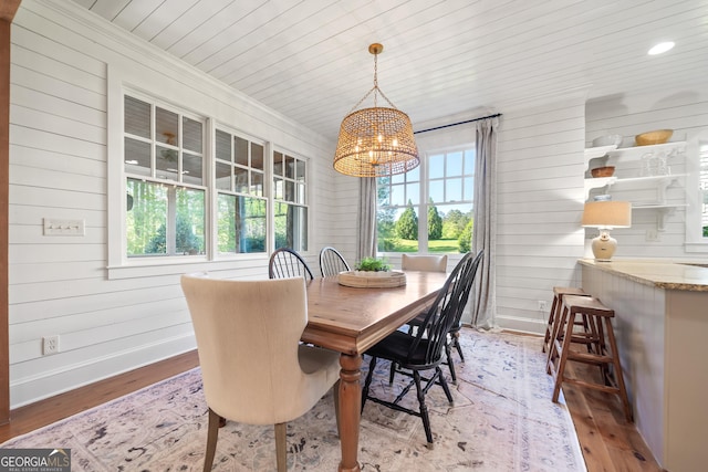 dining room with wooden walls, plenty of natural light, light wood finished floors, and a notable chandelier