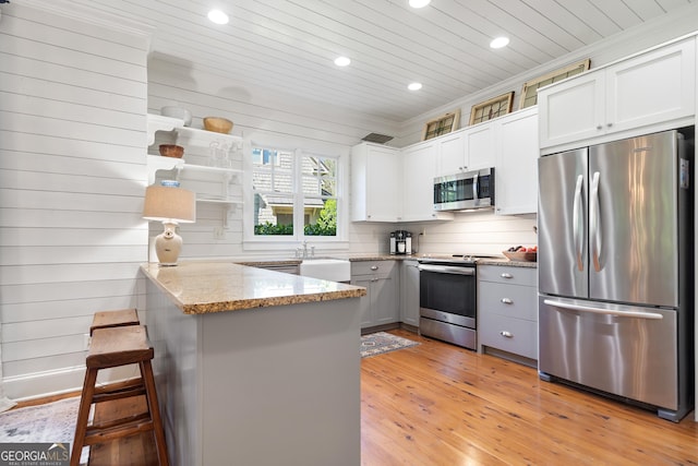 kitchen featuring recessed lighting, stainless steel appliances, light wood-type flooring, light stone countertops, and a peninsula