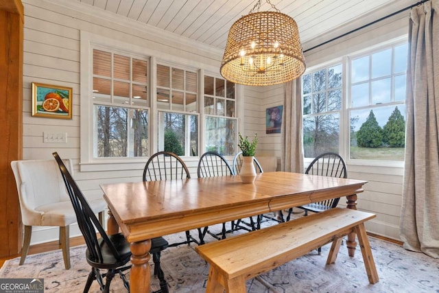 dining space with light hardwood / wood-style flooring, wooden walls, and a notable chandelier