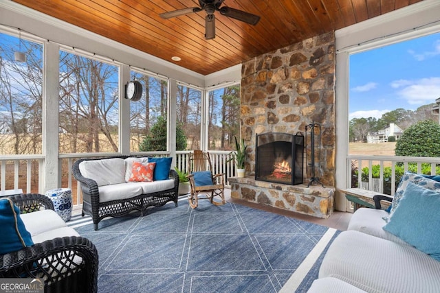 sunroom with ceiling fan, an outdoor stone fireplace, and wood ceiling