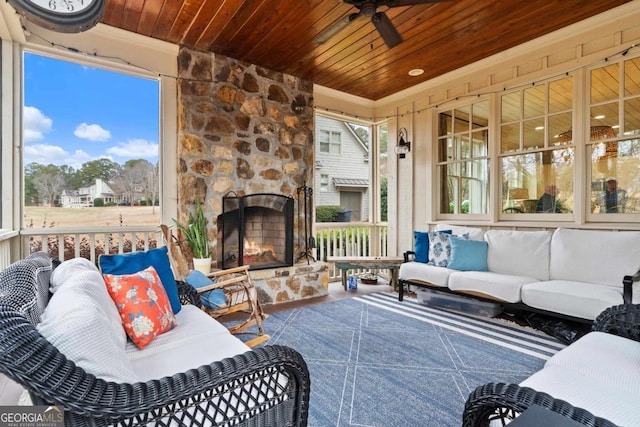 sunroom / solarium featuring ceiling fan, a healthy amount of sunlight, an outdoor stone fireplace, and wooden ceiling