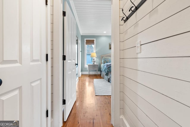 corridor with light hardwood / wood-style floors, crown molding, and wooden walls