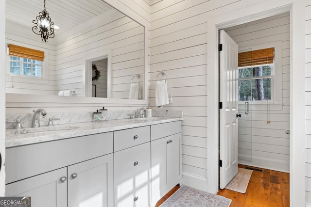full bath with wood finished floors, a sink, a chandelier, wooden walls, and double vanity