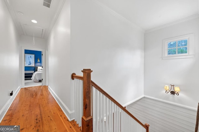 hall with attic access, light wood-type flooring, visible vents, an upstairs landing, and crown molding